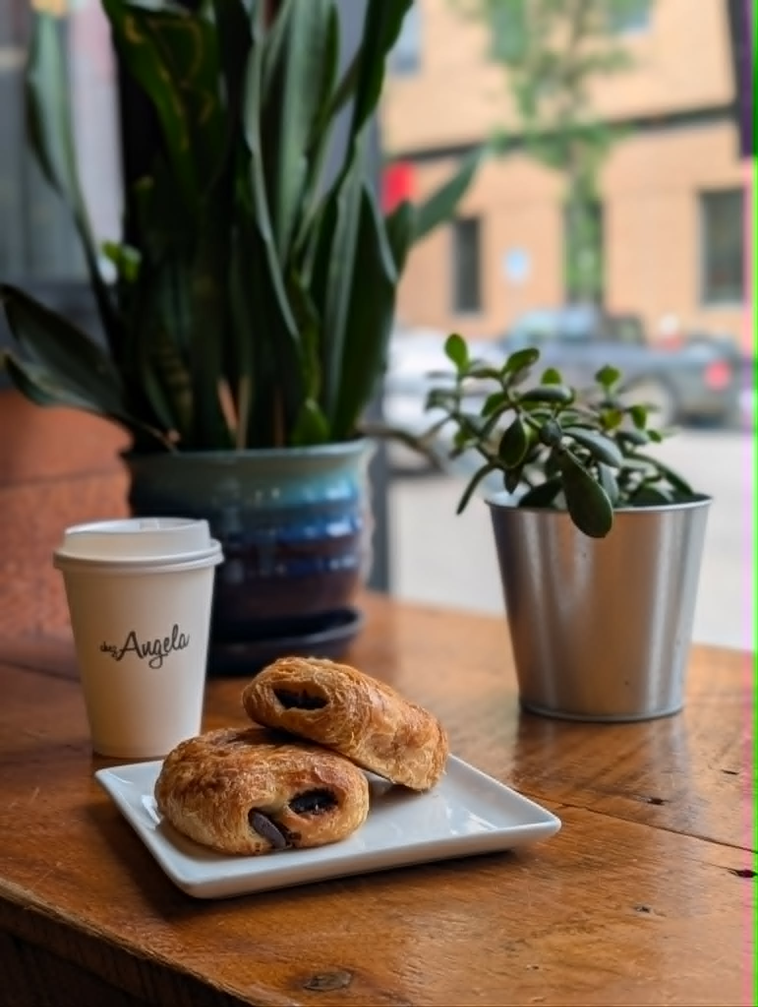 Chez Angela coffee cup, pastries, and plants on a warm café table